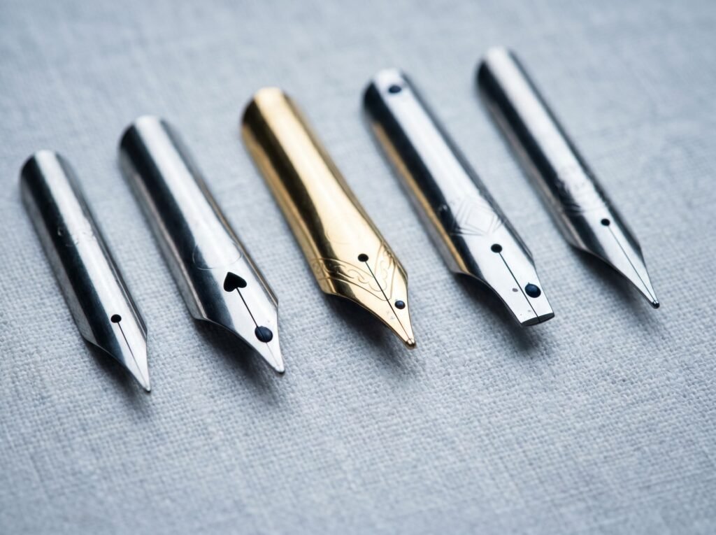 Five fountain pen nibs in different sizes and materials photographed from above on linen