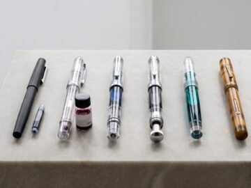 Six fountain pens showing different filling systems arranged on a grey stone surface