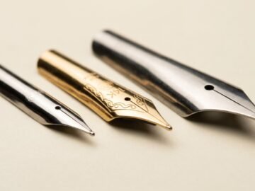 Three fountain pen nibs side by side showing steel, 14K gold, and broad nib shapes