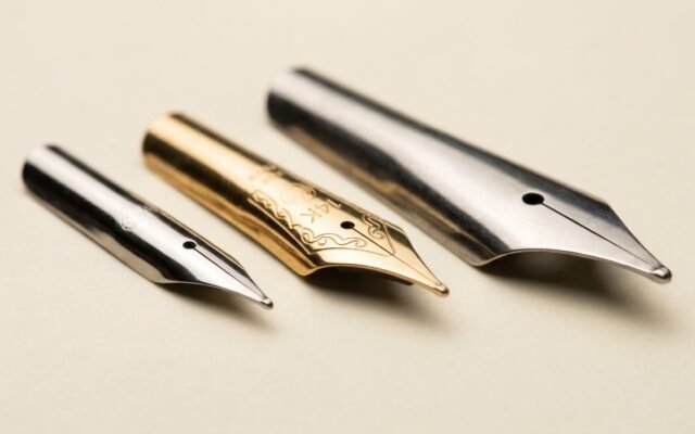 Three fountain pen nibs side by side showing steel, 14K gold, and broad nib shapes